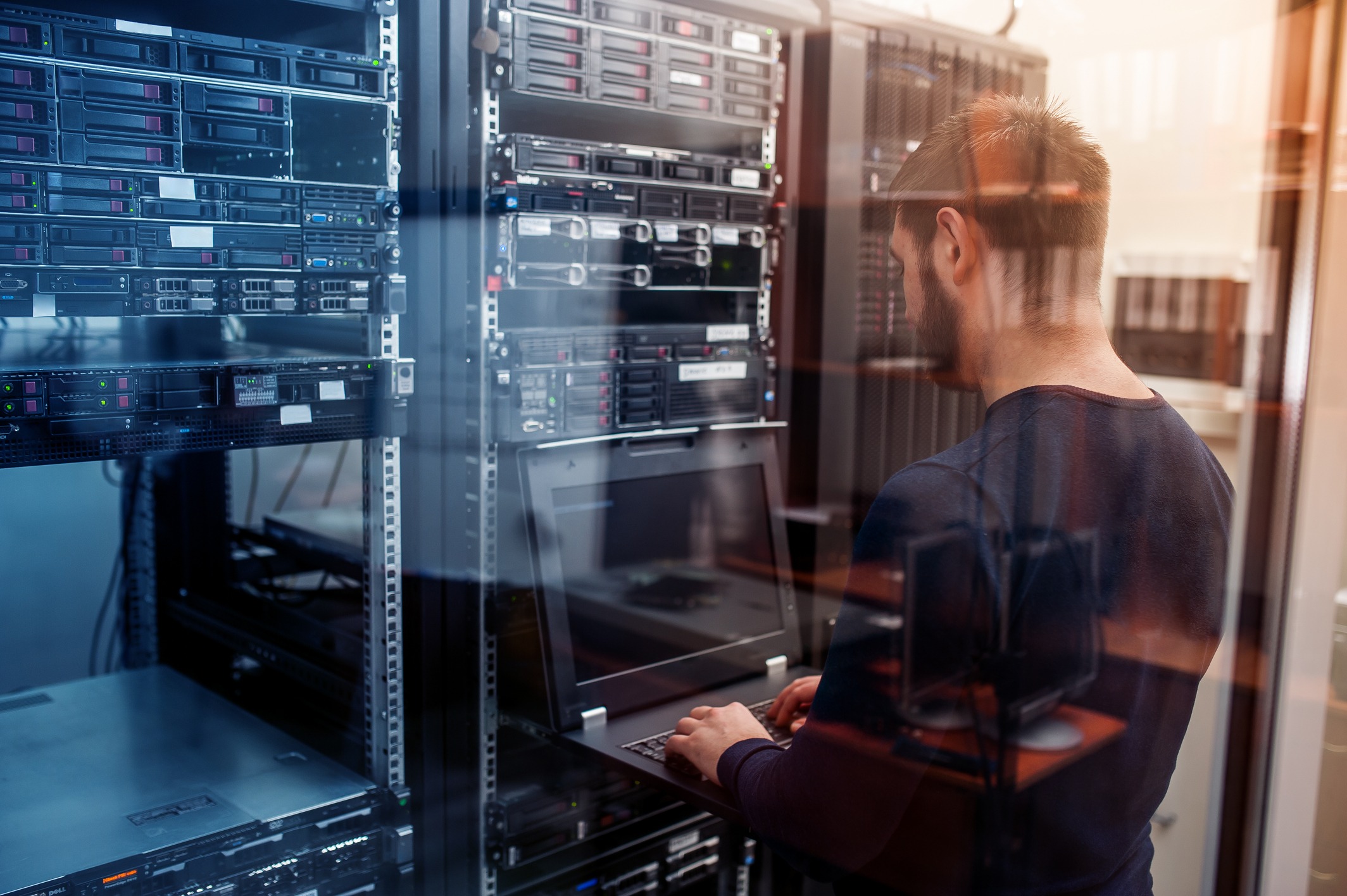 A technician operates a laptop in a server room filled with racks of servers, showcasing tech maintenance and infrastructure management.