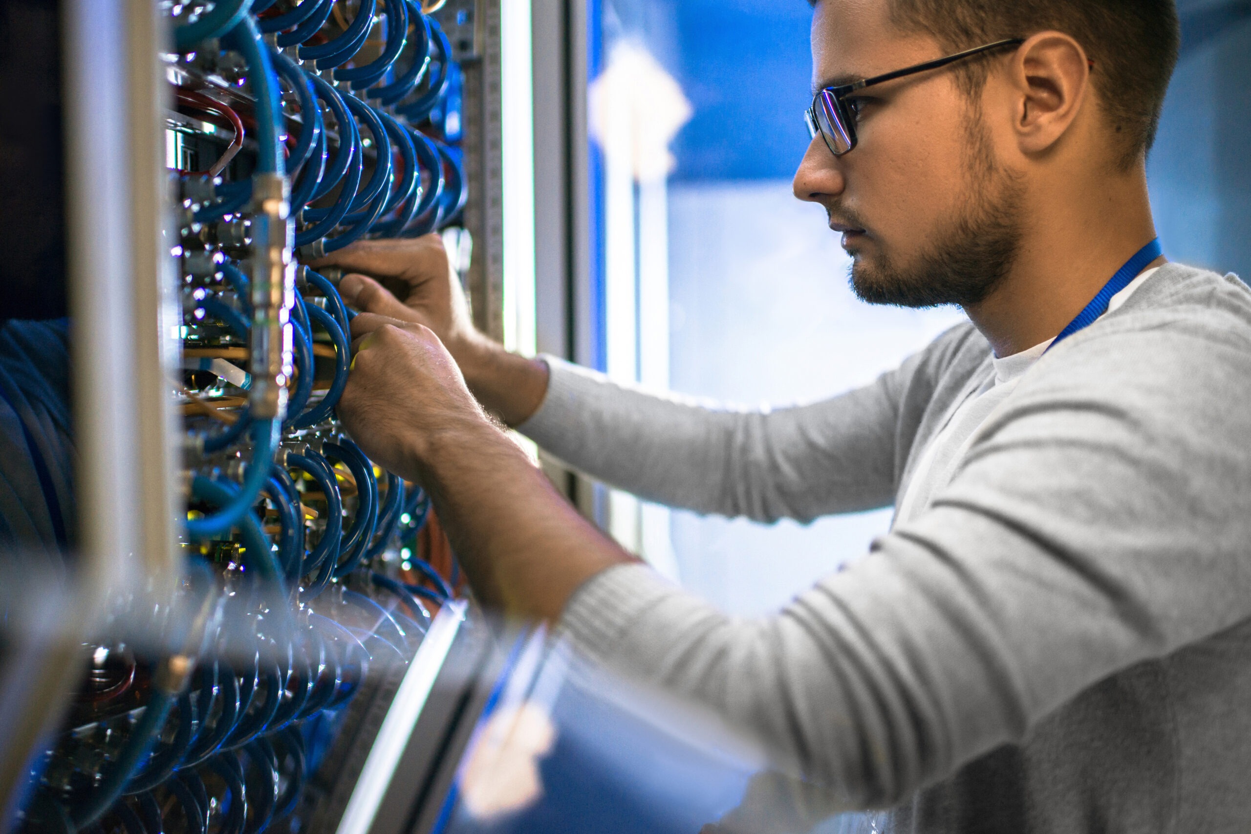 Technician adjusts blue cables in a server rack, focused on maintaining network infrastructure in a data center.
